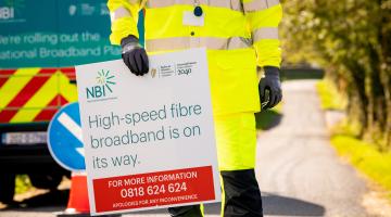 Worker holding a sign with "High speed broadband is on the way" wrote on it